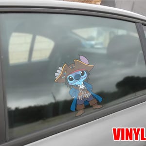 May include: A blue cartoon character wearing a pirate hat and costume, with the word "VINYL" in red block letters. The character is affixed to a car window, with a blurred background visible through the glass.