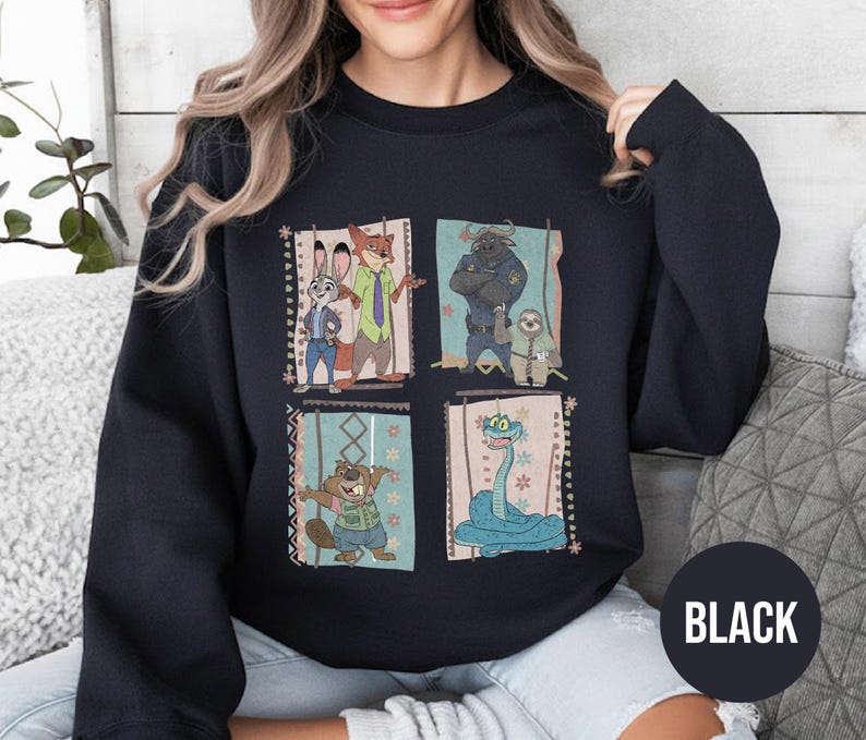 K&ouml;nnte beinhalten: Schwarzes Sweatshirt mit einem farbenfrohen Grafikdesign von Charakteren aus dem Animationsfilm Zoomania. Das Design umfasst Judy Hopps, Nick Wilde, Chief Bogo, Flash und andere. Das Wort "BLACK" ist auf einem schwarzen Kreis unten rechts aufgedruckt.