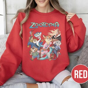 以下が含まれることがあります： 青と緑の文字で「Zootopia」という言葉が入った赤いクルーネックのトレーナー。 アニメ映画のキャラクターのカラフルなグラフィックが特徴です。 右下隅には「RED」という単語が入った赤い円があります。