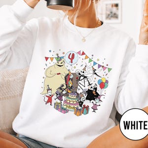 May include: White sweatshirt featuring a colorful cartoon birthday scene with characters, a cake, and the number 4 on a balloon. The word "WHITE" is in a white circle on the bottom right.