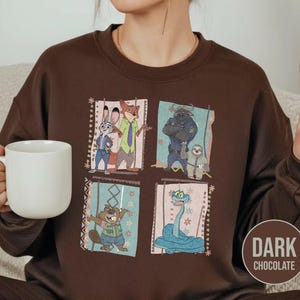 K&ouml;nnte beinhalten: Dunkel schokoladenbraunes Sweatshirt mit einem farbenfrohen Aufdruck von Charakteren aus dem Animationsfilm Zootopia. Das Design umfasst Judy Hopps, Nick Wilde, Chief Bogo, Flash und andere. Das Sweatshirt hat einen Rundhalsausschnitt und lange &Auml;rmel.