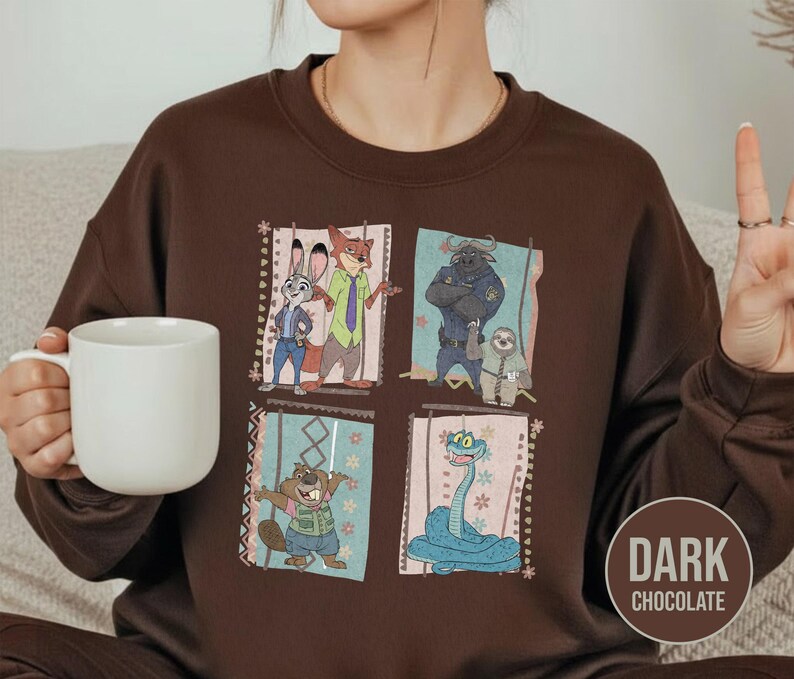 K&ouml;nnte beinhalten: Dunkel schokoladenbraunes Sweatshirt mit einem farbenfrohen Aufdruck von Charakteren aus dem Animationsfilm Zootopia. Das Design umfasst Judy Hopps, Nick Wilde, Chief Bogo, Flash und andere. Das Sweatshirt hat einen Rundhalsausschnitt und lange &Auml;rmel.