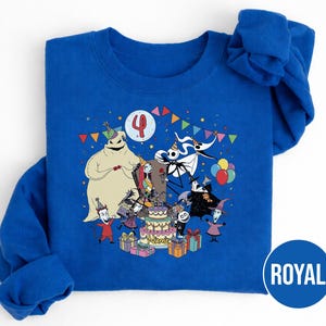 May include: Royal blue sweatshirt featuring a colorful graphic of characters from The Nightmare Before Christmas celebrating a birthday. The design includes a birthday cake, balloons, and the number 4. The word "NAME" is on the cake.