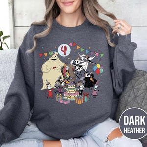 May include: Dark heather gray sweatshirt featuring a colorful graphic of characters from The Nightmare Before Christmas celebrating a birthday. The design includes a birthday cake, presents, and the number 4.