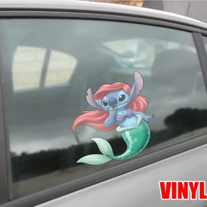 May include: A blue and pink cartoon character with a mermaid tail, resembling a Disney character, is featured on a car window. The character has pink hair, a blue body, and a green tail. The word "VINYL" is printed in red.