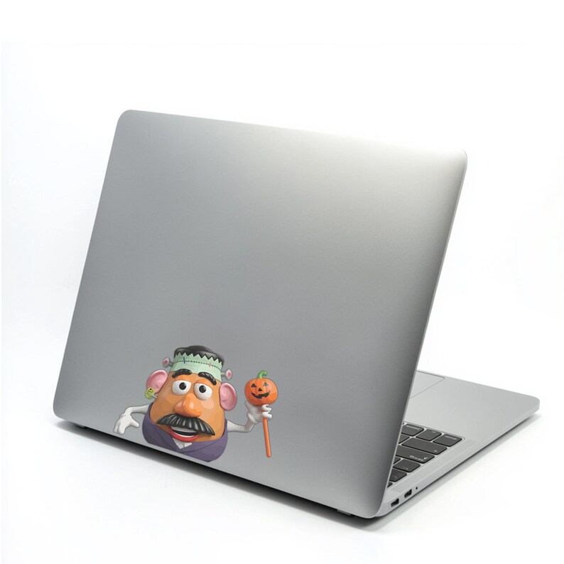May include: A silver laptop with a sticker of a cartoon Mr. Potato Head dressed as Frankenstein, holding a pumpkin lollipop. The sticker has a green and black hat, a large mustache, and a purple vest. The pumpkin is orange.