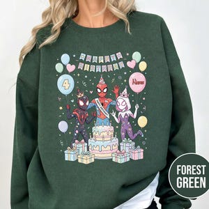 May include: Forest green sweatshirt featuring a colorful birthday graphic with Spider-Man characters. The design includes a cake, balloons, and the text "Happy Birthday." The number "4" is on a balloon. The sweatshirt is a comfortable, casual style.