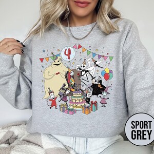 May include: Sport grey sweatshirt featuring a colorful graphic of characters from The Nightmare Before Christmas celebrating a birthday. The design includes a cake, presents, and the number 4. The sweatshirt has long sleeves and a crew neck.