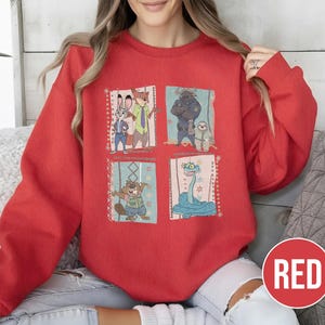 K&ouml;nnte beinhalten: Ein rotes Sweatshirt mit vier illustrierten Panels von Zeichentrickfiguren. Die Panels zeigen ein Kaninchen, einen Fuchs, einen B&auml;ren, ein Faultier, einen Biber und eine Schlange. Das Wort "RED" befindet sich in einem roten Kreis unten rechts.