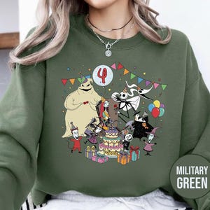 May include: Military green sweatshirt featuring a colorful graphic of characters from The Nightmare Before Christmas celebrating a birthday. The design includes a cake, balloons, and the number 4. The word "NAME" is on the cake.