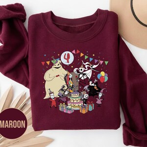 May include: Maroon sweatshirt featuring a colorful graphic of characters from a popular animated film celebrating a birthday. The design includes a birthday cake, presents, and the number 4. The sweatshirt has long sleeves and a crew neck.