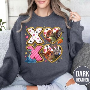 May include: Dark heather gray sweatshirt featuring a graphic design with the letters "XO" and heart-shaped images of cartoon characters. The design includes a snake, a fox, a bunny, and a donkey. The sweatshirt is made of a soft material.