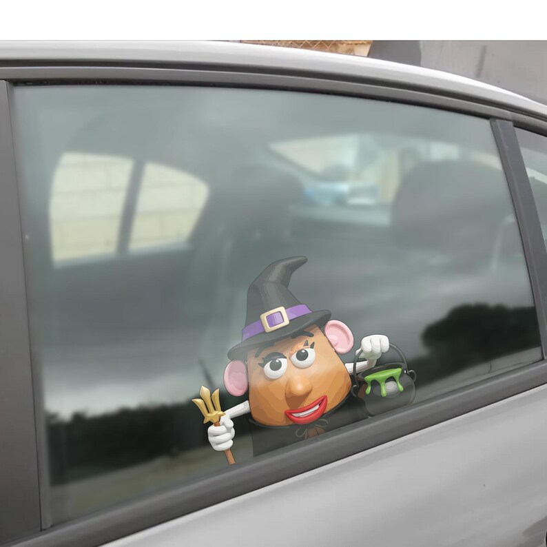 May include: A whimsical Halloween car decoration featuring a potato-shaped character dressed as a witch. The character wears a black hat with a purple band and holds a trident and a cauldron. The decoration is designed to attach to a car window.