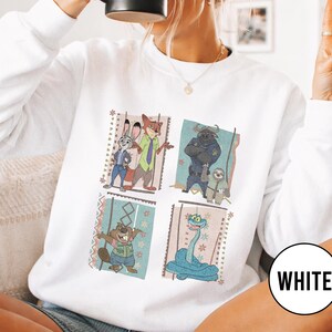 K&ouml;nnte beinhalten: Wei&szlig;es Sweatshirt mit vier quadratischen Tafeln mit Zeichentrickfiguren. Die Tafeln zeigen Judy Hopps und Nick Wilde, Chief Bogo und Flash, einen Biber und eine blaue Schlange. Das Wort "WHITE" ist auf einem wei&szlig;en Kreis aufgedruckt.