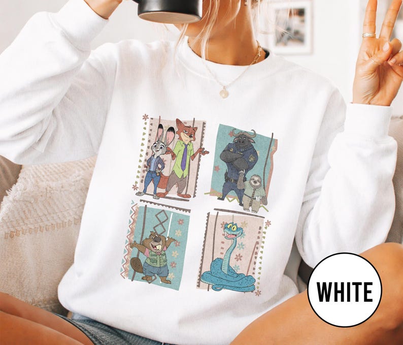 K&ouml;nnte beinhalten: Wei&szlig;es Sweatshirt mit vier quadratischen Tafeln mit Zeichentrickfiguren. Die Tafeln zeigen Judy Hopps und Nick Wilde, Chief Bogo und Flash, einen Biber und eine blaue Schlange. Das Wort "WHITE" ist auf einem wei&szlig;en Kreis aufgedruckt.