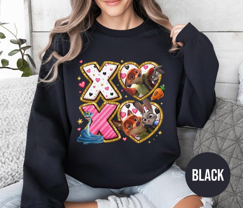 May include: Black sweatshirt featuring a graphic design with the letters "XO" in gold glitter and pink. The design includes cartoon characters in heart-shaped frames. The word "BLACK" is printed on a black circle.