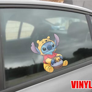 May include: A vinyl car decal featuring the character Stitch from Lilo & Stitch, dressed in a Winnie the Pooh costume, holding a honey pot. The decal is in full color and is applied to a car window.