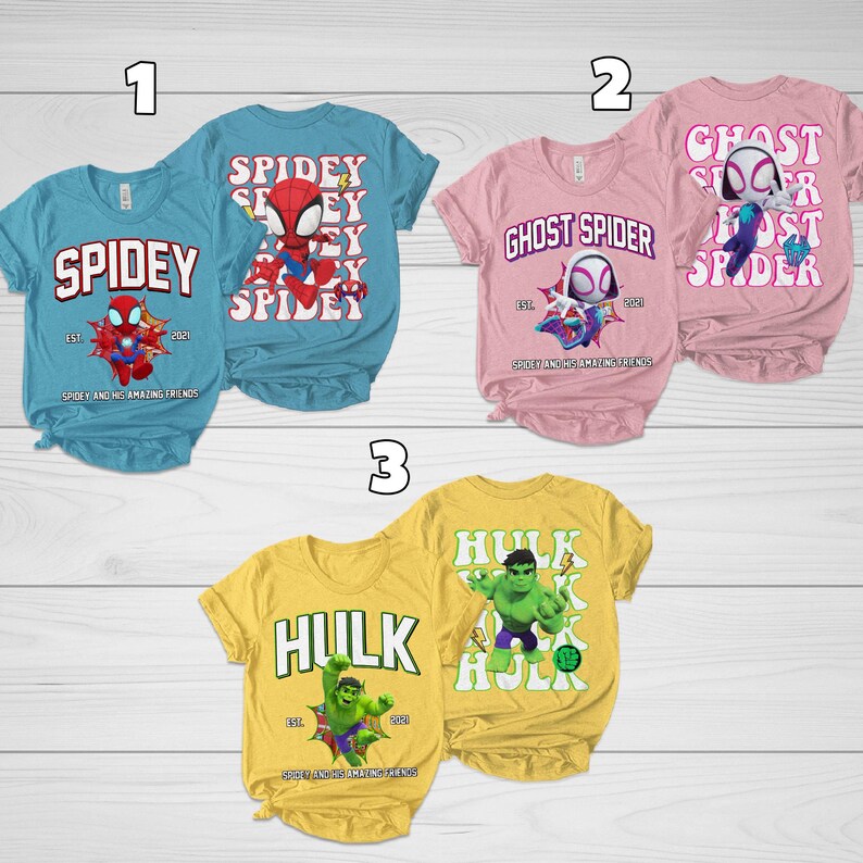Puede incluir: Una colecci&oacute;n de tres camisetas de manga corta con dise&ntilde;os de superh&eacute;roes. Las camisetas son de color azul claro, rosa y amarillo. Cada camiseta tiene un gr&aacute;fico y texto de superh&eacute;roe diferente, incluyendo "Spidey", "Ghost Spider" y "Hulk".