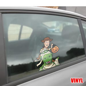 May include: A colorful vinyl decal featuring Woody from Toy Story holding a jack-o'-lantern treat bag, riding on a green dinosaur wrapped in bandages. The word "VINYL" is in the bottom right corner.