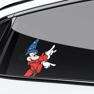 May include: A colorful car decal featuring Mickey Mouse in a wizard costume. Mickey is wearing a blue wizard hat with stars and a red robe. His white gloved hands are pointing to the right. The decal is applied to a car window.