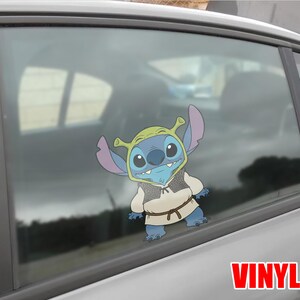 May include: A blue cartoon character wearing a green hat and a tan vest, with a brown belt, is affixed to a car window. The word "VINYL" is printed in red at the bottom right.