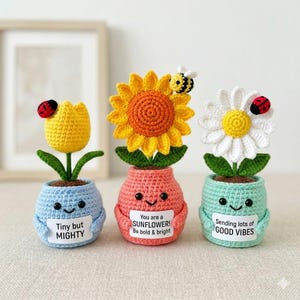 May include: Three crocheted flower pot decorations. A yellow tulip with a ladybug, a sunflower with a bee, and a daisy with a ladybug. Each pot is a different color and has a positive message on a small sign.