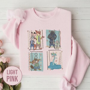 K&ouml;nnte beinhalten: Hellrosa Sweatshirt mit einem farbenfrohen Aufdruck von Charakteren aus dem Animationsfilm Zoomania. Das Design umfasst Judy Hopps, Nick Wilde, Chief Bogo, Flash und andere. Das Sweatshirt ist aus weichem Material.