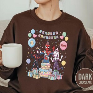 May include: Dark chocolate brown sweatshirt featuring a colorful graphic of Spider-Man characters celebrating a birthday. The design includes a cake, balloons, and the words "Happy Birthday". The number "4" is on a balloon.