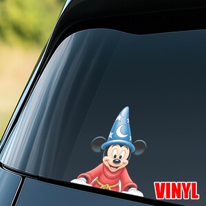 May include: A vinyl decal featuring Mickey Mouse in a sorcerer's outfit, with a blue hat adorned with stars and a crescent moon. Mickey is wearing a red robe. The word "VINYL" is in red.