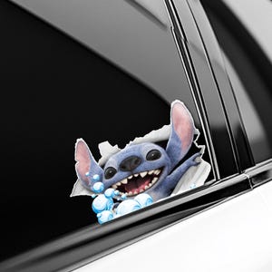 Puede incluir: Un personaje de dibujos animados azul, Stitch, irrumpe a trav&eacute;s de una superficie blanca, con una gran sonrisa y burbujas. El personaje tiene orejas grandes y una expresi&oacute;n amigable. La imagen es una calcoman&iacute;a para coche.