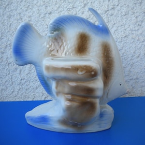 Könnte beinhalten: Keramik-Fisch-Dekoration in Blau und Weiß mit braunen Akzenten. Der Fisch hat eine kleine Öffnung auf dem Rücken. Das Objekt steht auf einer blauen Oberfläche. Dekoratives Element.