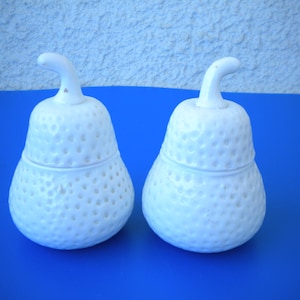 May include: Two white ceramic pear-shaped containers with lids. The containers have a textured surface that resembles a pear skin.