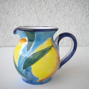 Peut inclure: Un petit pichet en céramique bleu et blanc avec un motif de citron jaune. Le pichet a une anse et un corps arrondi.