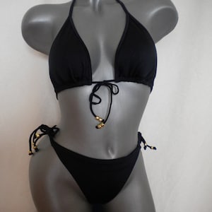 May include: Black bikini top and bottom with gold bead accents. The top is a triangle style with adjustable straps. The bottom is a tie-side style.