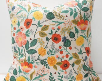 May include: A square decorative pillow with a floral pattern. The pillow features a cream-colored background with a repeating pattern of red, orange, yellow, and pink flowers, green leaves, and small blue butterflies. The pillow is a home decor item.