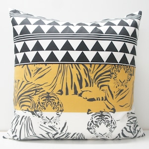 Puede incluir: Una almohada decorativa con un patrón geométrico blanco y negro en la parte superior, una franja amarilla con siluetas de tigres negras en el medio y una franja blanca con siluetas de tigres negras en la parte inferior.
