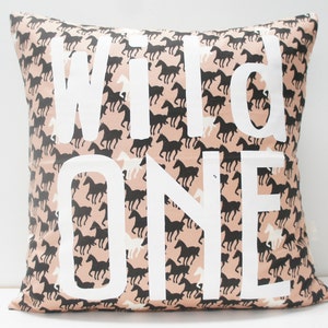 May include: A pink pillow with a black and white horse print. The pillow has the words "Wild One" printed in white on the front.