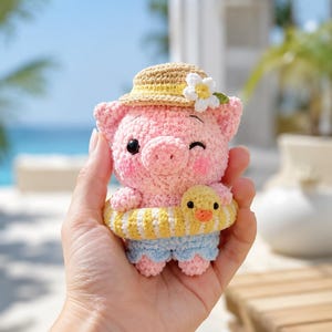 Peut inclure: Une petite figurine de cochon crochetée rose portant un chapeau de paille beige avec une fleur blanche, un short bleu clair et une bouée rayée jaune et blanche avec une petite tête de canard jaune fixée à l'avant de la bouée.