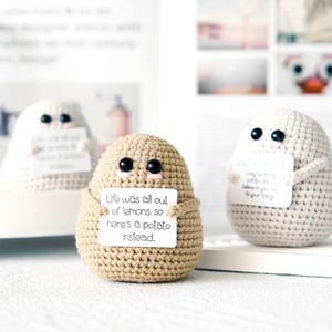 Puede incluir: Tres figuras de patata de ganchillo, cada una con ojos de botón negros y pequeños acentos rosas. La patata central sostiene un letrero que dice "Life was all out of lemons, so here's a potato instead."