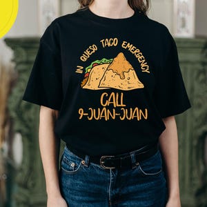 May include: A black t-shirt with a graphic of two tacos and the text "In Queso Taco Emergency Call 9-Juan-Juan".