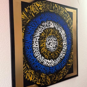 May include: A square canvas painting with a black background and a gold frame. The painting features a circular design with concentric circles of blue, white, and gold. The circles are made up of stylised letters and symbols.
