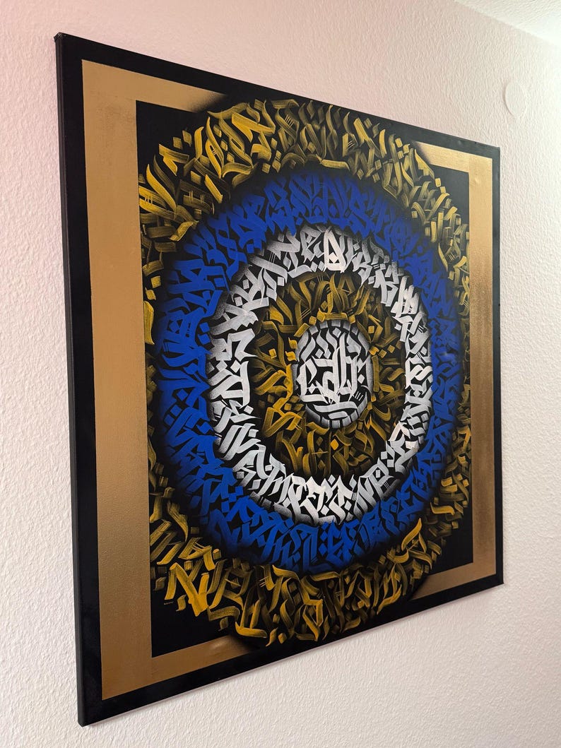 May include: A square canvas painting with a black background and a gold frame. The painting features a circular design with concentric circles of blue, white, and gold. The circles are made up of stylised letters and symbols.