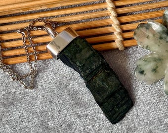 May include: A dark green, rectangular, textured raw stone pendant suspended from a thin silver-toned metal chain. The stone features a rough, layered surface and is secured by a polished silver-toned metal cap at the top of the pendant.