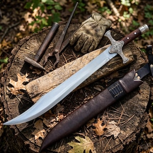 Könnte beinhalten: Ein Stahlschwert mit geschwungener Klinge und verziertem silberfarbenem Parierstange, mit einem dunklen Holzgriff und Metallakzenten. Daneben liegen eine dunkelbraune Lederscheide mit schwarzer Schnürung, ein abgenutzter beiger Lederhandschuh und Werkzeuge.