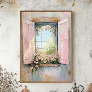 Puede incluir: Pintura enmarcada de una ventana abierta con contraventanas rosas y una vista de un jardín. El alféizar está lleno de flores rosas y el cielo es azul. La obra de arte tiene un estilo suave e impresionista con un marco de madera.