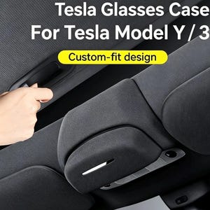 Könnte beinhalten: Ein dunkelgraues Brillenetui, das an der Innenverkleidung eines Fahrzeugdachs montiert ist. Der Text lautet Tesla Glasses Case For Tesla Model Y / 3 und Custom-fit design. Das Etui hat eine stoffbezogene Oberfläche mit einer schmalen Akzentlinie.