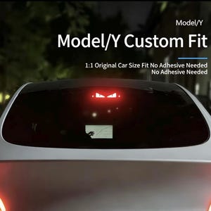 Può includere: Vista posteriore di un'auto argentata con un accessorio su misura. Il testo "Model/Y Custom Fit" è visualizzato sopra il lunotto. Sotto, si legge "1:1 Original Car Size Fit No Adhesive Needed". È visibile una luce rossa con un design a occhio.