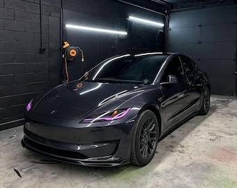 Puede incluir: Un sedán gris oscuro con ventanas tintadas y luces de acento moradas en los faros. El vehículo presenta un diseño de carrocería aerodinámico y elegante con llantas negras de radios múltiples, estacionado en un garaje con paredes negras.