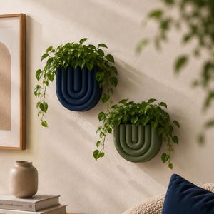 May include: Two semi-circular wall-mounted planters featuring a ribbed, arch-like design. One planter is dark navy blue and the other is olive green. Both containers hold lush green trailing plants with heart-shaped leaves.
