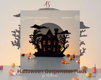 May include: A black laser-cut silhouette of a haunted house with a chimney, surrounded by two bare trees and clouds against a large circular moon backdrop. The house features illuminated windows. Scattered candy corn pieces are in the foreground.
